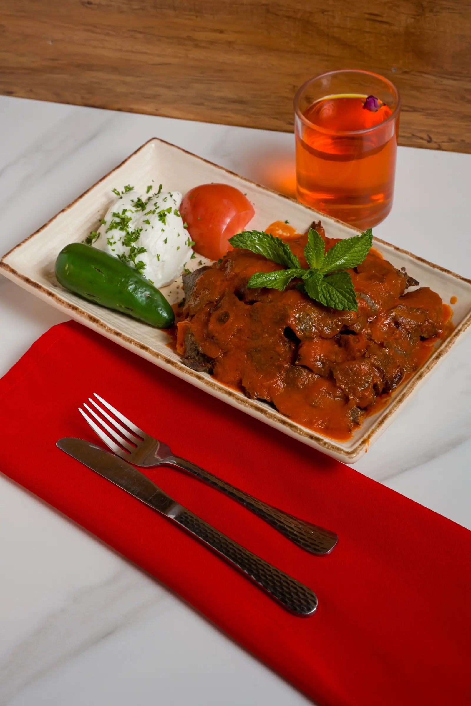 Lamb topped with tomato sauce, accompanied by yogurt, grilled pepper, and tomato