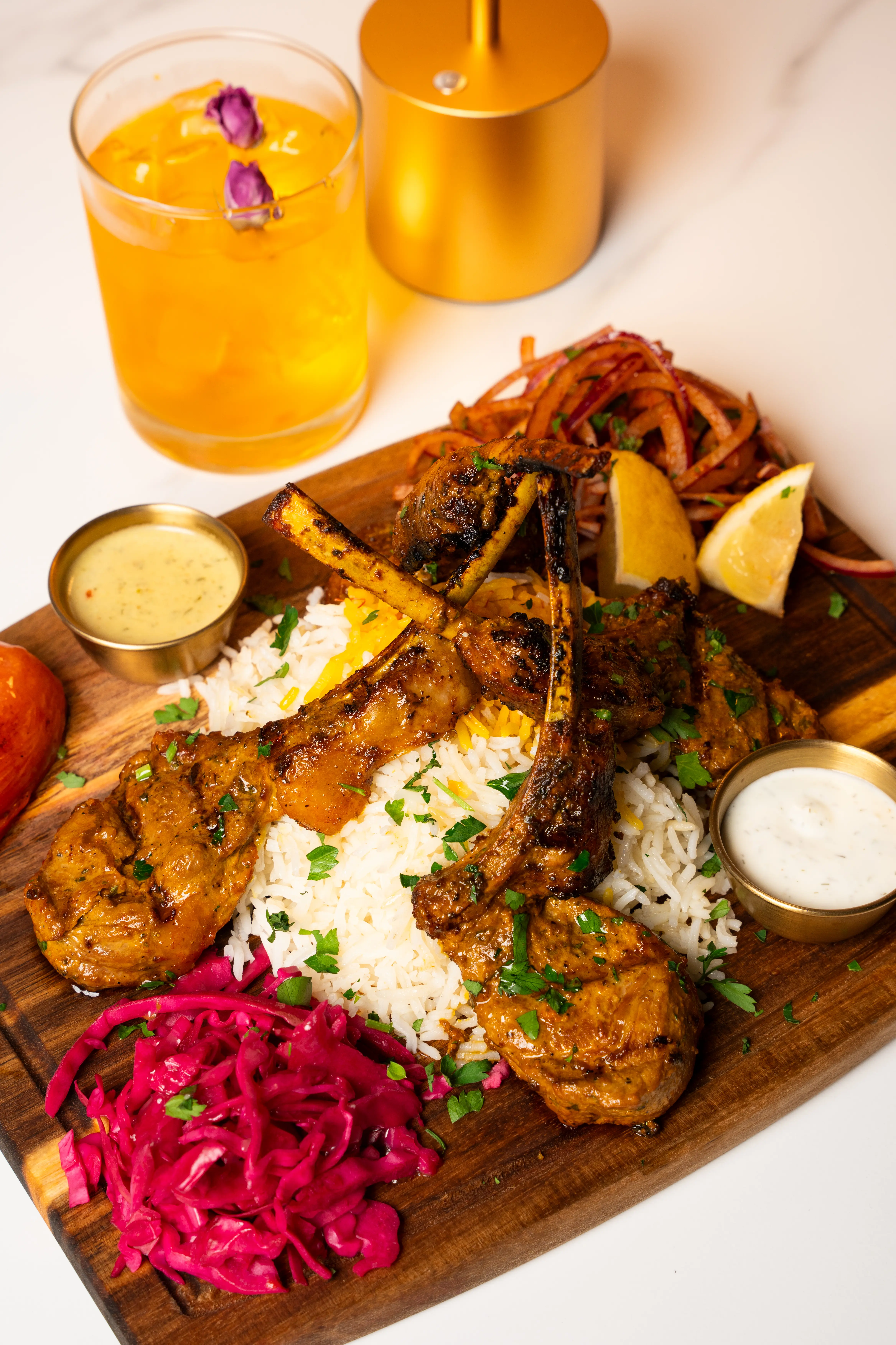 Mixed grill platter with lamb chops, kebab, koobideh, rice, and sauces on wooden board