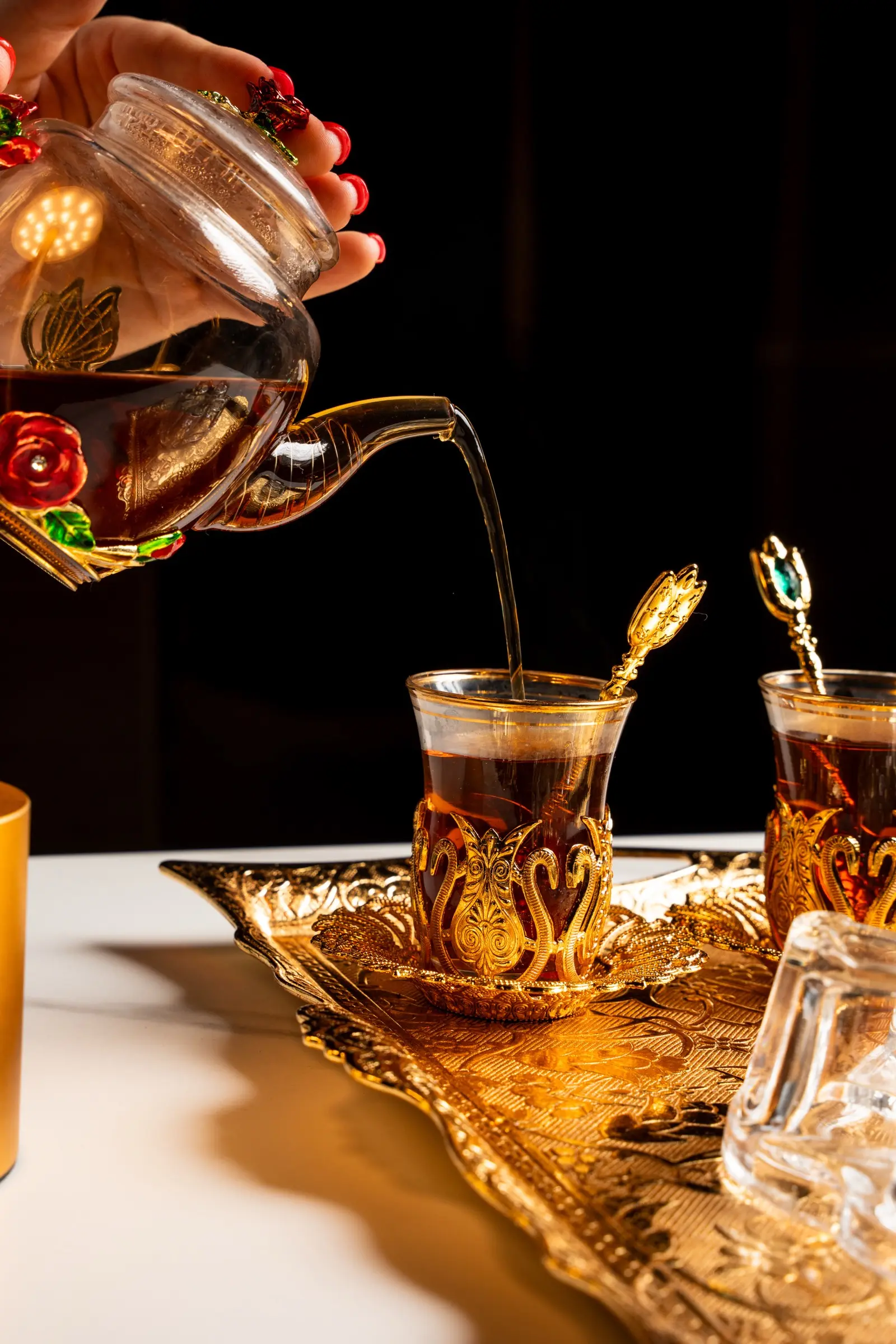 Hot tea being poured from an ornate glass teapot into a gold-filigreed tulip glass
